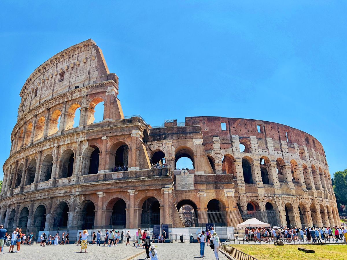 The curved outer wall of the Colosseum rising above a busy plaza in Rome